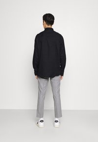 Camisa negra de manga larga con cuello puntiagudo y puños de botón, combinada con pantalones grises claros ajustados y zapatillas blancas.