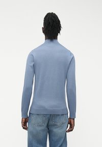 Svetlo modra pletena majica z visokim ovratnikom, dolgimi rokavi in rebrastimi robovi, kombinirana s svetlopranimi denim kavbojkami.