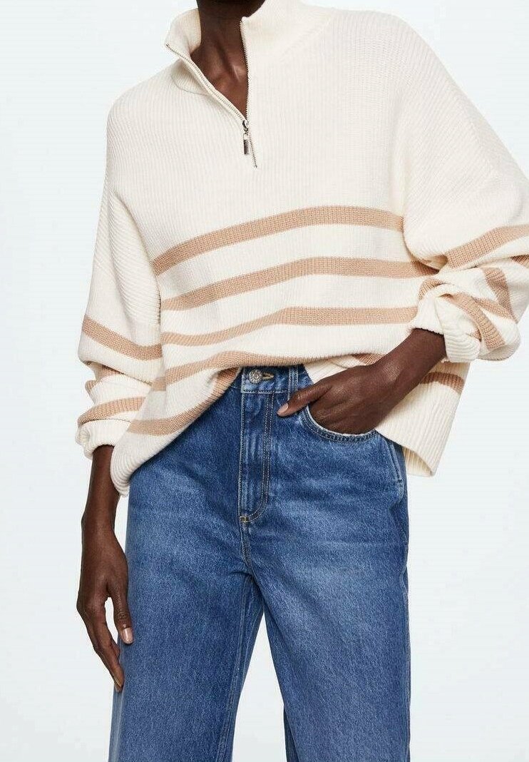 Pull crème à col, avec des rayures beige horizontales et une texture côtelée. Associé à un jean bleu taille haute et coupe droite.
