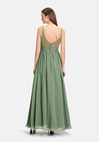 Robe de soirée longue verte avec un dos nu, ornée de broderies complexes sur un corsage transparent et une jupe fluide. Tissu en chiffon lisse.