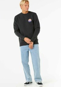 Donkergrijze sweatshirt met een rond grafisch logo, gecombineerd met lichtblauwe jeans en zwarte sneakers. Eenvoudig ontwerp, rechte pasvorm, van katoen.
