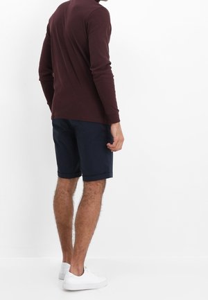 Mørk burgunder langærmet skjorte, marineblå shorts og hvide sneakers. Skjorten har en ribbet tekstur, slim fit og rund hals.