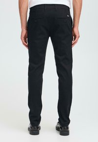 Zwarte broek met een recht model, gemaakt van geweven stof. Details zijn onder andere twee achterzakken met knoopsluitingen.