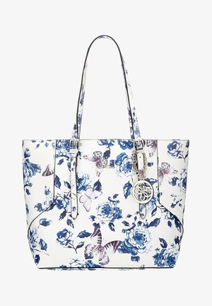 Sac fourre-tout blanc avec imprimé floral bleu et papillon violet, double poignées, breloque en métal doré, et logo Guess sur le devant.