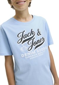 Camiseta de algodón azul claro con mangas cortas. En la parte frontal presenta un logo impreso "Jack & Jones" en blanco y negro, con acentos gráficos.
