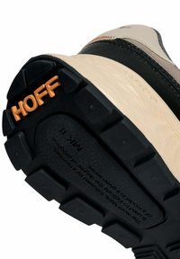 Suola di sneaker beige e nera con battistrada nero spesso, marchio arancione "HOFF" e testo in rilievo sulla suola intermedia.