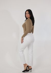 Dopasowana, beżowa bluzka z długim rękawem połączona z białymi, wysokim stanem jeansami. Stylizację dopełniają czarne sandały na obcasie z przeźroczystymi paskami.