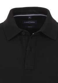 Svart polotröja gjord av stretchmaterial; har krage, tvåknappslå och en etikett med "CASA MODA" och storlek "M."