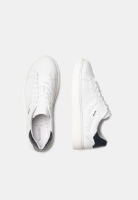 Sneaker bianche in pelle con un design minimalista, suola in gomma piatta e accenti blu navy sul tallone e sui pannelli laterali.