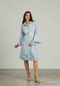 Blaues Hemdkleid mit taillierter Taille und Glockenärmeln. Verfügt über ein Spitzenmuster im Rautendesign. Getragen mit tanfarbenen Espadrille-Wedges.