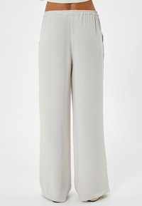 Pantalon large gris clair avec une taille élastique, présentant une texture lisse et douce et des poches sur les côtés, offrant une coupe décontractée.