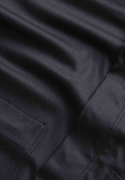 Marinblått tyg med en matt yta, med subtila veck och en fickdetalj, som visar en jämn textur och rena sömmar.