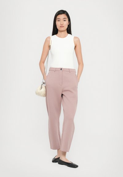 Λευκή εφαρμοστή αμάνικη μπλούζα, ανοιχτό ροζ κομμένα παντελόνια με πλαϊνές τσέπες, και μαύρες επίπεδες παπούτσια. Κρατάει μια μικρή κρέμ τσάντα.