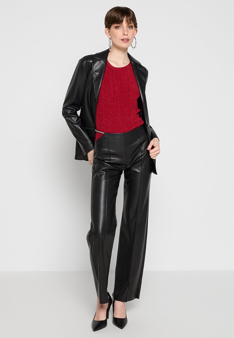 Zwarte faux leren blazer over een rode textuurtop, gepaard met hoge taille, zwarte faux leren rechte broeken en zwarte hoge hakken.