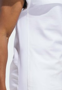 Top blanco sin mangas con una textura suave, que presenta un detalle en la costura lateral y un diseño ajustado. Sin patrones ni herrajes visibles.