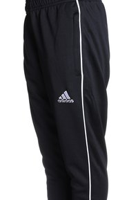 Czarne sportowe spodnie z fakturowanej tkaniny, z białym paskiem po boku i haftowanym logo na dolnej części nogawki. Elastyczny pasek w talii z kieszeniami.