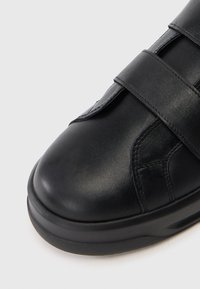 Crne kožne cipele s zaobljenim vrhom, sa dva podesiva Velcro remena i teksturiranom površinom. Potplat je blago podignut i izdržljiv.