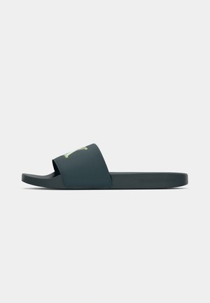 Mørkeblå glidesandal med en bred rem. Glat tekstur, minimalistisk design, med en grøn logoaccent på remmen.