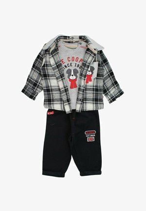 Chemise grise avec un motif de chien, veste en flanelle à carreaux noir et blanc, et pantalon en denim foncé avec des accents brodés et des poignets repliés.