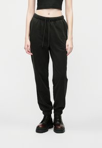 Čierne nohavice na jogging vyrobené z jemného materiálu, s elastickým pásom so sťahovacou šnúrkou, zúženými nohavicami a manžetami na koncoch.