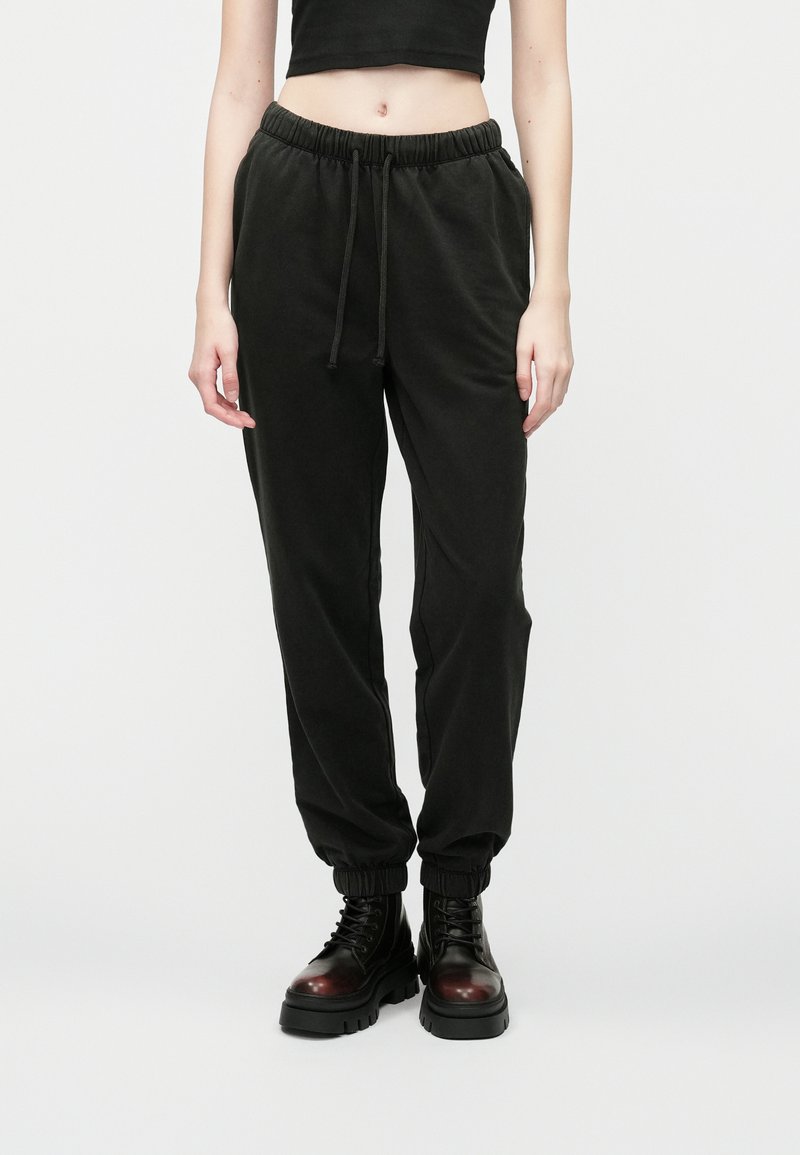 Čierne nohavice na jogging vyrobené z jemného materiálu, s elastickým pásom so sťahovacou šnúrkou, zúženými nohavicami a manžetami na koncoch.