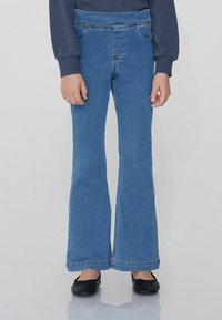 Niebieskie dżinsy w kształcie dzwonów z średnim stanem, z przednimi kieszeniami i jasnymi przeszyciami. Miękka tkanina dżinsowa o gładkiej fakturze.