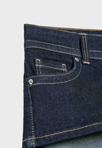 Jeans in denim scuro con una vita standard, caratterizzati da una piccola tasca frontale e cuciture a contrasto lungo le cuciture. Texture liscia.