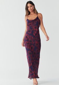 Maxi šaty z lehké, splývavé látky; mají fialový základ s velkými červenými květinovými motivy. Tenká ramínka a boční rozparky pro snadný pohyb.