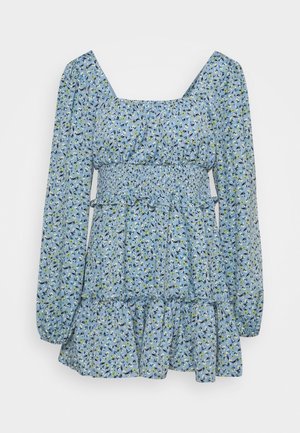 Mini-robe bleue à manches longues avec petit imprimé floral, taille smockée, encolure carrée et ourlet à volants sur un fond clair uni.