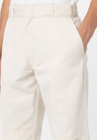 Pantalones de algodón beige con corte recto, que cuentan con bolsillos laterales, trabillas para el cinturón y un detalle de costura mínima. Textura suave y diseño resistente.