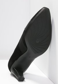 Scarpa nera con tacco alto, dotata di una tomaia in camoscio e di una suola in gomma testurizzata, caratterizzata da un design sagomato per comfort e stabilità.