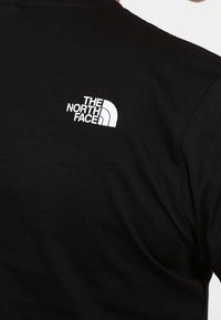 Tissu noir avec un logo blanc "THE NORTH FACE" sur le haut du dos, présentant le design demi-dôme de la marque.