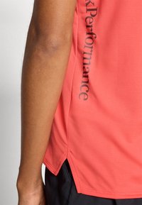 Coral performance tank top with textured fabric, side slits for ventilation, and black printed text along the shoulder seam.