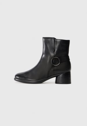Black ankle boots made of smooth leather, featuring a round toe, a low heel, and a side strap with a circular metal accent.