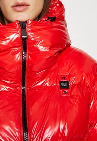 Doudoune brillante rouge vif avec col montant zippé, ornée d'un patch logo Blauer U.S.A. noir et blanc sur la poitrine.