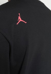 Černé tričko s krátkým rukávem a červeným logem Jumpman na levém rameni. Vyrobeno z měkké tkaniny s přiléhavým střihem.