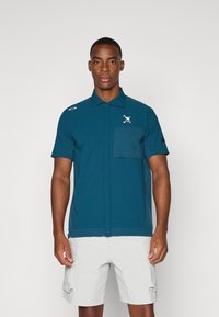 Teal short-sleeve shirt with a button-up design, featuring a chest pocket and a logo on the collar. Smooth fabric with a fitted cut.