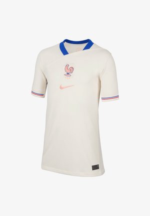Cremefarget fodboldtrøje med korte ærmer, blå krave og røde samt blå striber på ærmerne, prydet med et haneemblem og Nike-logo i pink.