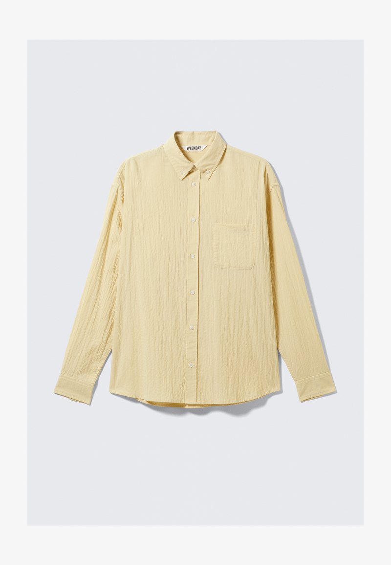 Yellow long-sleeve button-up shirt made of textured fabric, featuring a chest pocket, pointed collar, and rounded hem. Brand label visible.