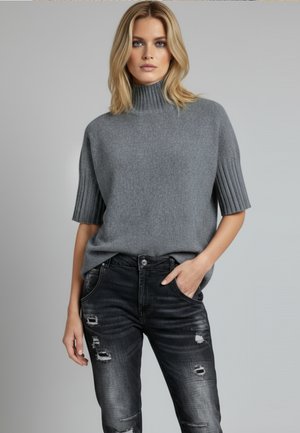 Grauer Strickpullover mit gerippten kurzen Ärmeln und hohem Kragen. Kombiniert mit schwarzen Jeans im Used-Look mit verschiedenen Rissen.