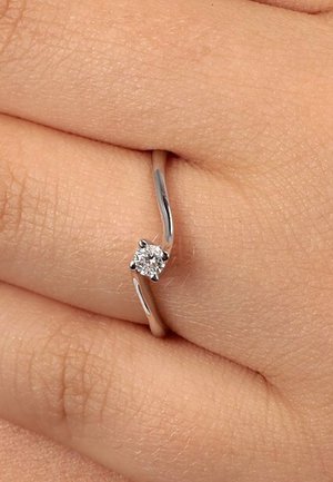 Silver ring with a twisted band featuring a round diamond set in six prongs, displayed on a hand with a textured skin background.