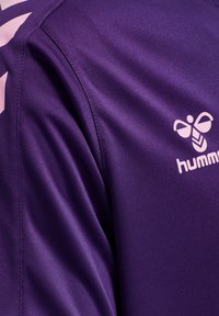 Fioletowy materiał na sportową koszulkę z logo pszczoły Hummel i paskami w jodełkę na ramieniu w jasnoróżowym kolorze.