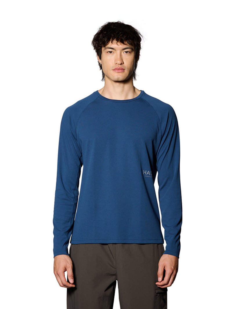 Man draagt een blauw atletisch shirt met lange mouwen en donkere broek, staand met het gezicht naar voren tegen een witte achtergrond.