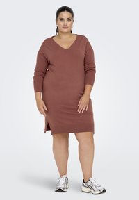 Roodkleurige gebreide jurk met V-hals en lange mouwen, met zijsplitten en geribde zoom. Draag met witte en zwarte sneakers.
