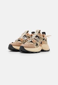 Sneakers chunky avec une tige en maille beige et beige clair, accents gris et noir, semelle en caoutchouc épaisse et fermeture à lacets avec des étiquettes de logo.