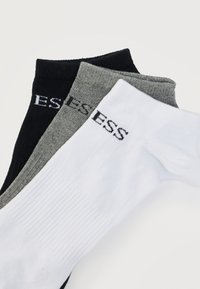 Trzy pary skarpet w kolorach czarnym, szarym i białym. Każda ma prążkowaną teksturę i logo nadrukowane w pobliżu mankietu.