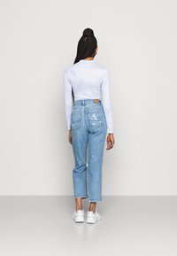 Haut blanc à longues manches au design ajusté, associé à un jean taille haute déchiré bleu clair et des baskets blanches.