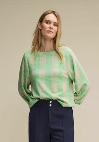 Lekka, długosleeve'owa bluzka w beżowym kolorze w zieloną kratkę. Miękka tekstura, luźny krój, okrągły dekolt, w połączeniu z granatowymi spodniami o wysokim stanie.