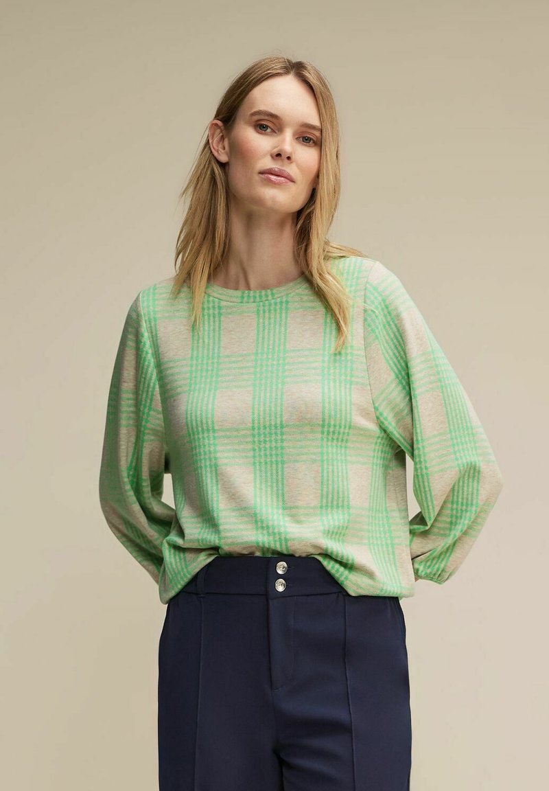 Lekka, długosleeve'owa bluzka w beżowym kolorze w zieloną kratkę. Miękka tekstura, luźny krój, okrągły dekolt, w połączeniu z granatowymi spodniami o wysokim stanie.