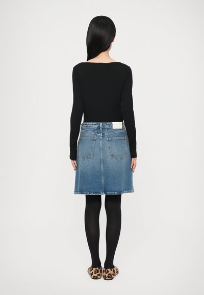 Black long-sleeve top, blue denim A-line skirt with back pockets, paired with black tights and leopard print slippers. Simple, structured design.